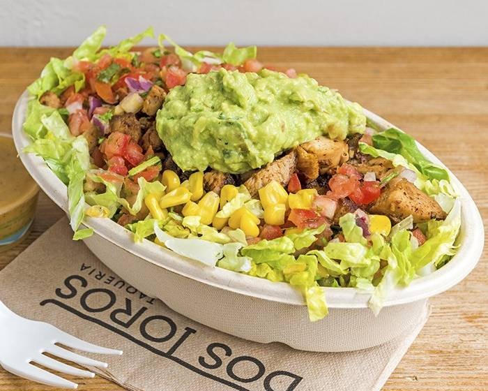 A bowl of salad with shredded lettuce, corn, salsa, meat, and guacamole, sitting on a Dos Toros paper napkin.