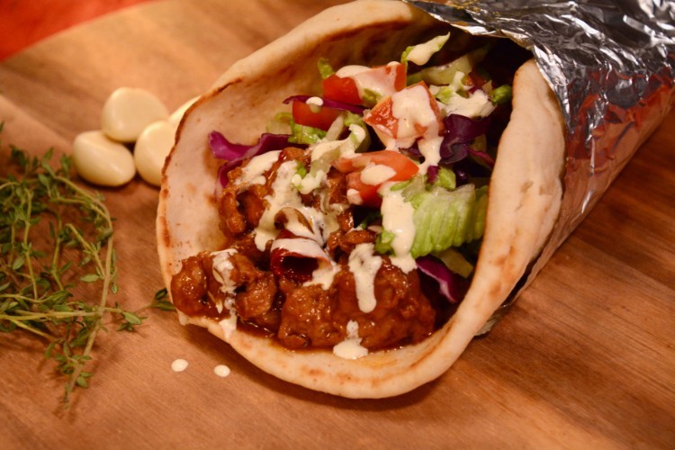 A pita bread with sauced meat and letttuce and dressing.