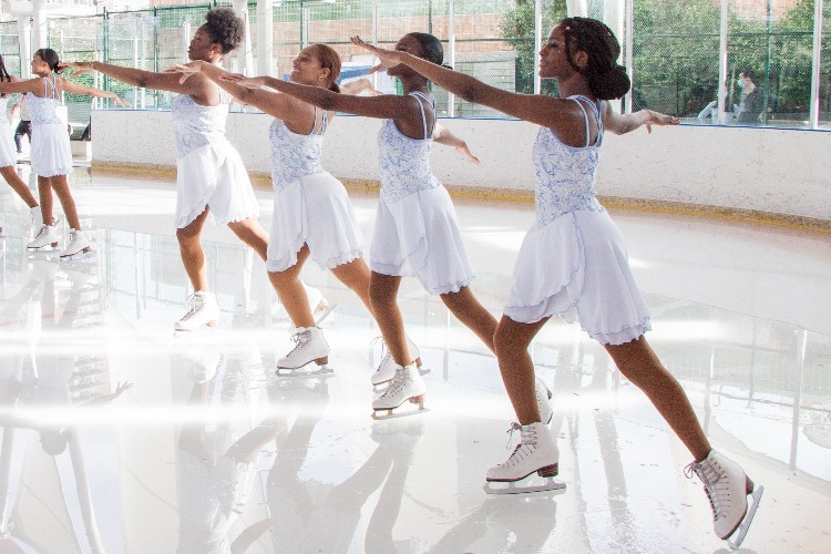 A group of young women in white figure skating dresses skate in sync.