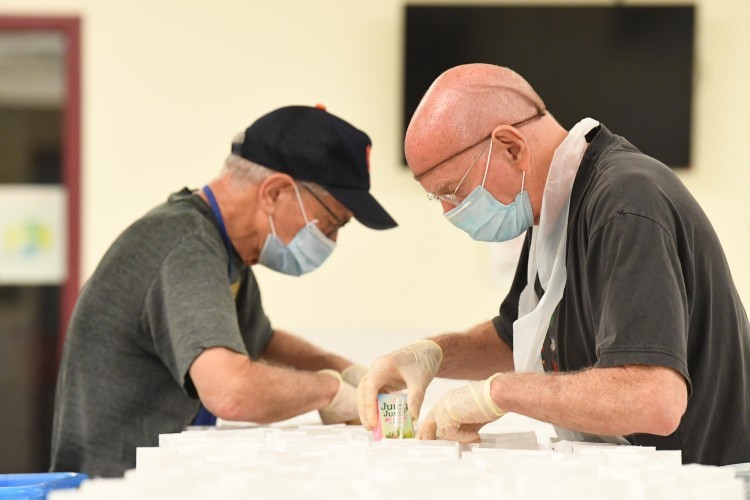 Two men putting food items in white paper bags.