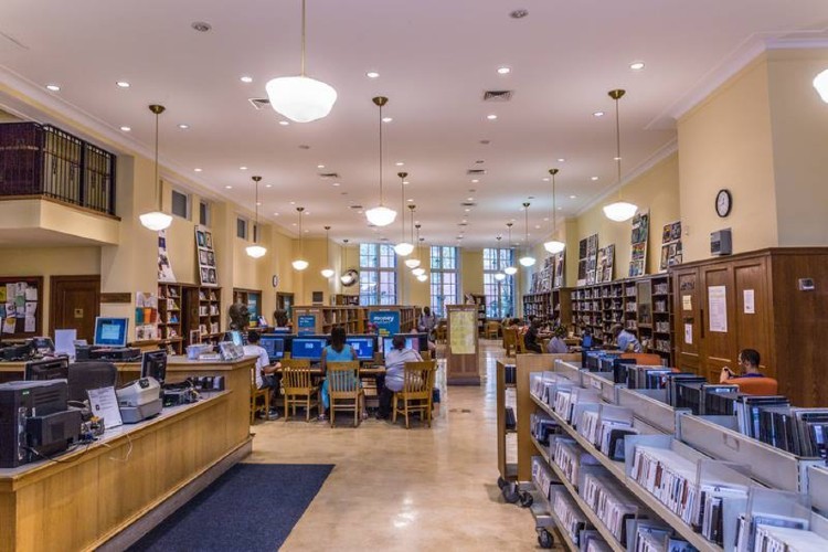 The inside of a library, with circulation desks and patrons using computers visible.