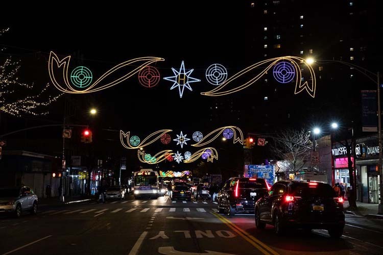 Holiday lights are strung across 125th Street in Harlem with cars moving underneath.