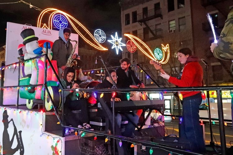 A parade float with people playing instruments and holiday lights in the background.