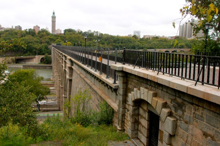 A stone bridge with a walkway on top and a tower in the distance