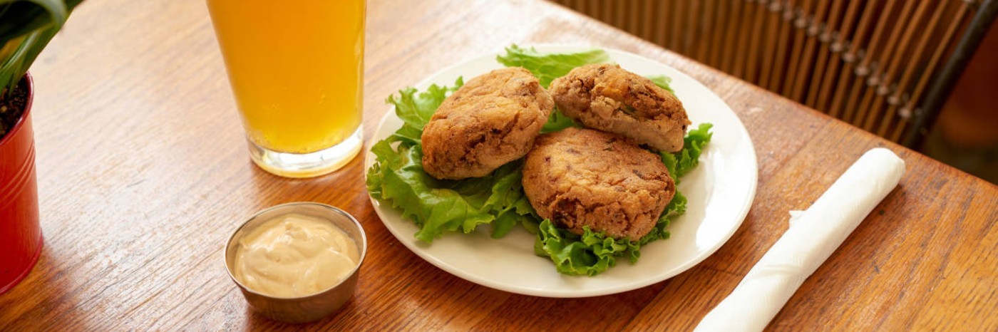 Fried patties on a bed of lettuce on a plate, with a drink and a container of sauce on the side.