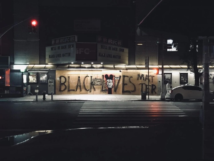 A nighttime streetscape with "Black lives matter" spray painted on plywood covering a storefront.