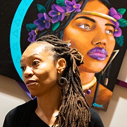 A woman speaking to a group of people in front of a painting. 