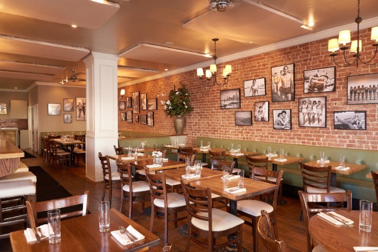 The interior of a restaurant with an exposed brick wall behind the tables and black and white photos on the wall