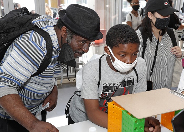 A father and son in face masks look at a computer