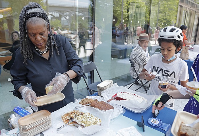 A visitor enjoys a sample from Chatman J Cakes, a Columbia-Harlem Small Business Development Center client. Photo by Lou Rocco. A kid in a NASA shirt and helmet tastes cake.