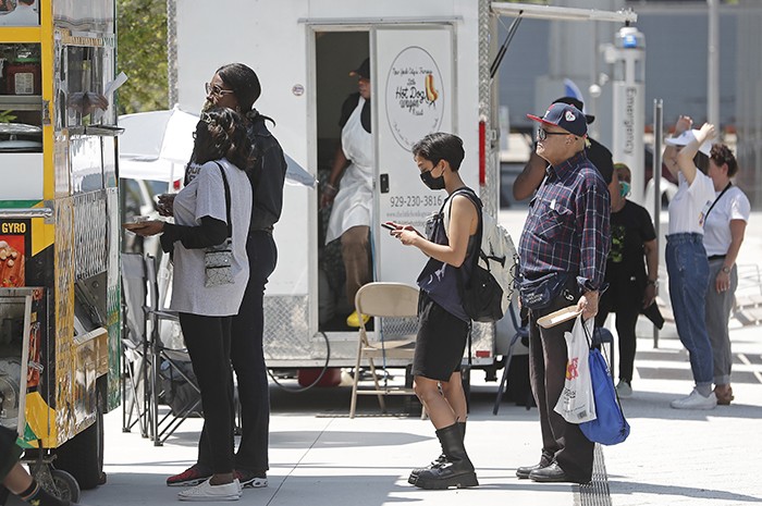 Patrons line up at two food trucks, Fauzia's Heavenly Delights and the Little Hot Dog Wagon.