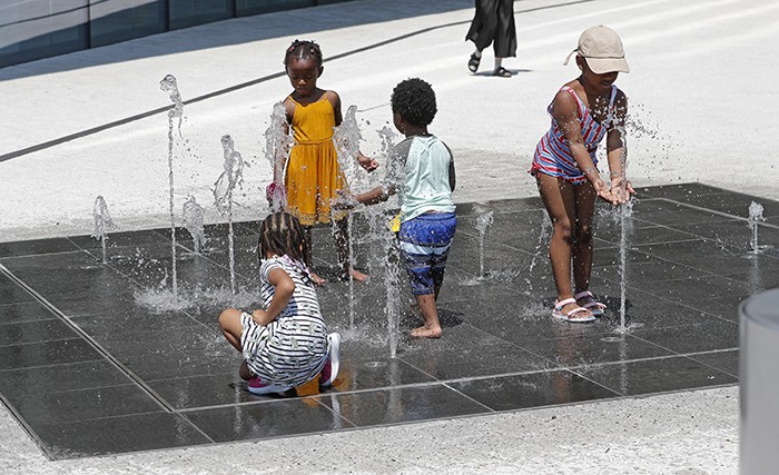 Children play on a splash pad in front of Kravis Hall