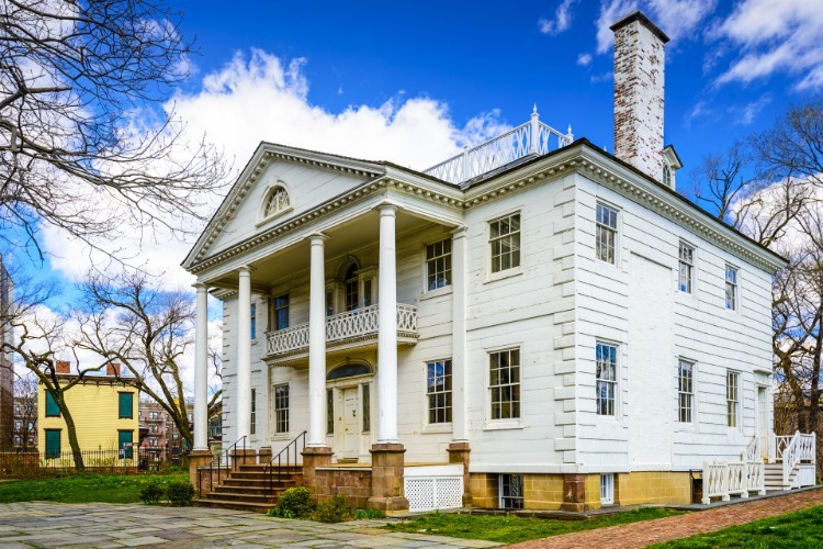 A large white house on a stone foundation against a blue sky.