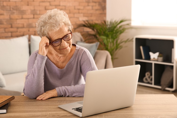 An older woman in a purple shirt looks at a laptop.