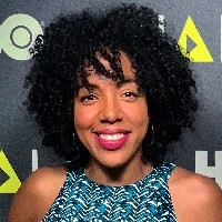 A woman with natural hair and a blue shirt smiles at the camera.