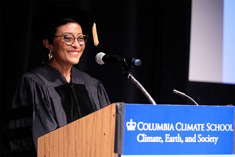 Peggy Shepard in a black cap and gown addresses the audience from a podium with "Columbia Climate School" written on it.