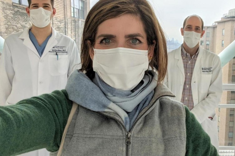 COVID-19 survivor Diana Berrent with Kevin Roth, MD, PhD, and Eldad Hod, MD. Photo credit: Diana Berrent. A woman wearing a surgical mask taking a selfie with doctors in white coats and surgical masks visible behind her.
