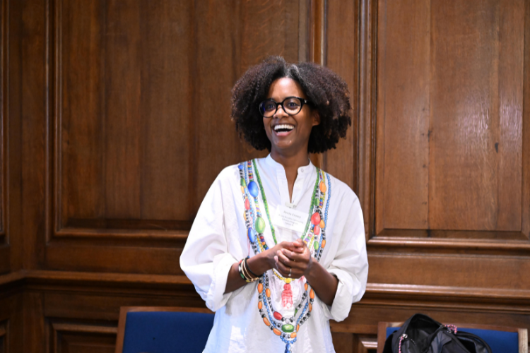 Renita Croney, a member of the 11th cohort, introduces her research project. Photo by Eileen Barroso. A woman laughs while speaking to the crowd.