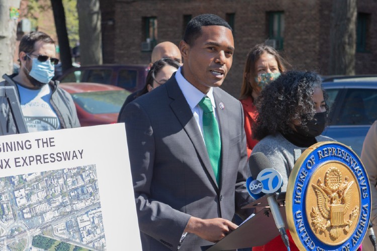 Rep. Richie Torres standing at a U.S. House of Representatives lectern with an aerial view of the Cross Bronx Expressway on a poster.