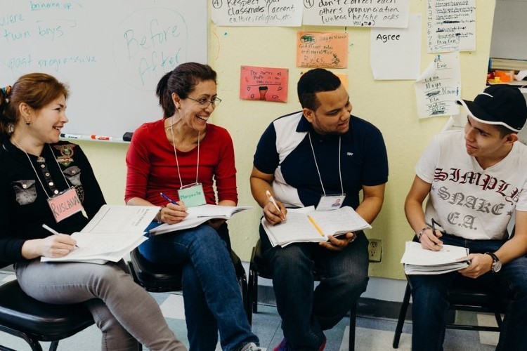 Four adult language students with name tags and notebooks talk to each other.