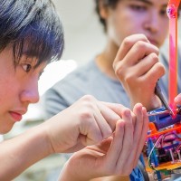 Two teen boys work on a small mechanism.