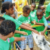 A group of children petting a goat.