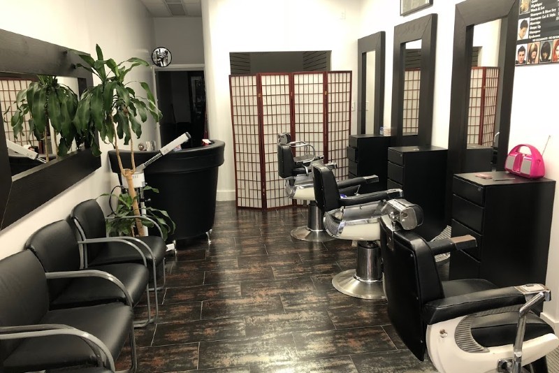 The inside of a salon with black waiting chairs on the left side and three chairs for haircuts on the right side.