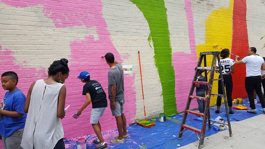 A group of adults and children painting a brick wall that will become the "From Harlem with Love" mural.