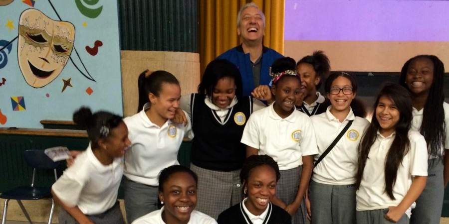 Young students in matching white shirts smiling and laughing with an adult engineer standing behind them and laughing.