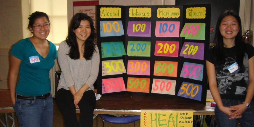Three college-aged women who volunteer with HEAL and a jeopardy board with topics on alcohol, tobacco, marijuana, and potpourri.
