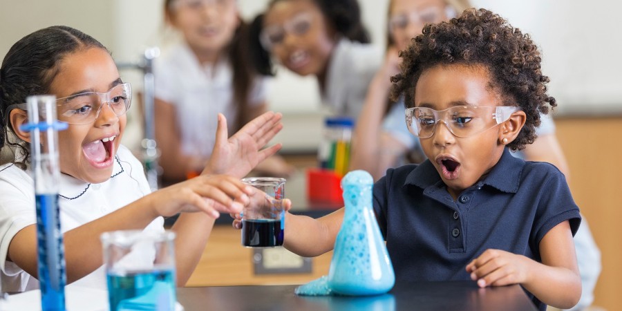 Two young children using beakers full of liquid to do a science experiment.
