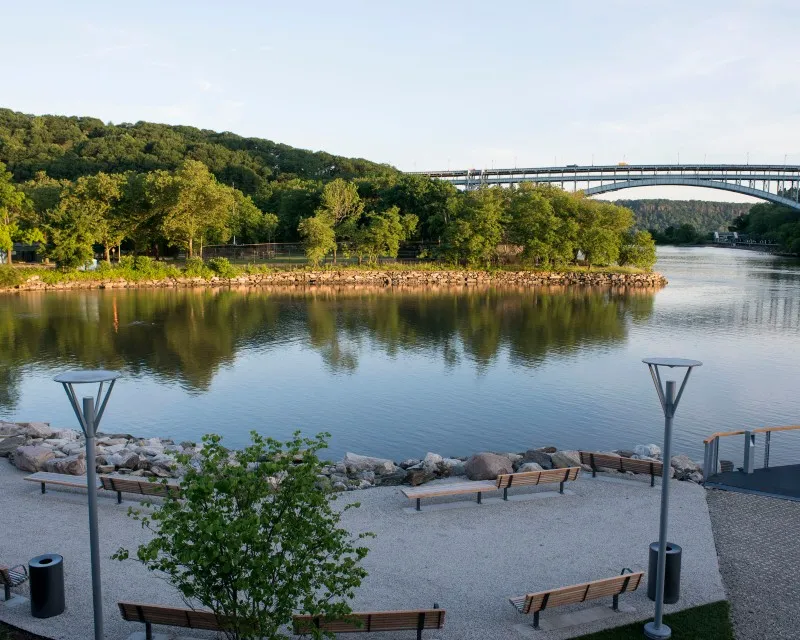 A park with a body of water, trees and bridge.