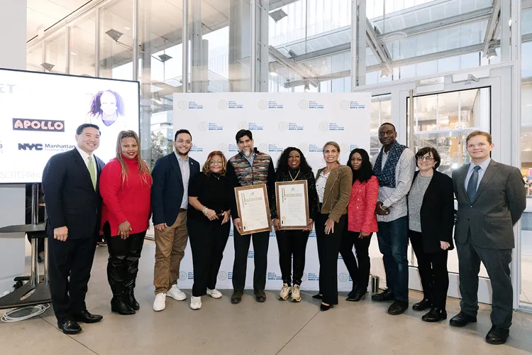 A group of Uptown NYC community leaders posing for a photo in The Forum, the two people in the middle are holding an award.