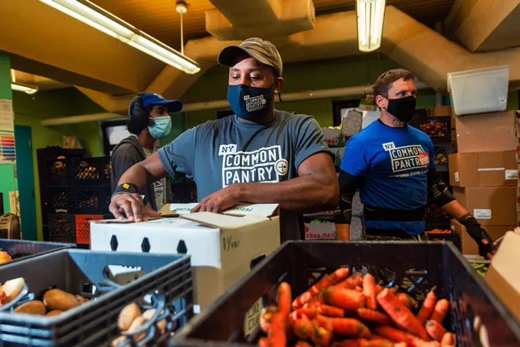 Three masked volunteers packing boxes of produce to be given out at New York Common Pantry locations throughout the city.