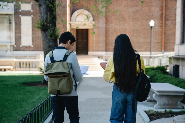 Two young students with backpacks on walking on a concrete path on Columbia's campus. 