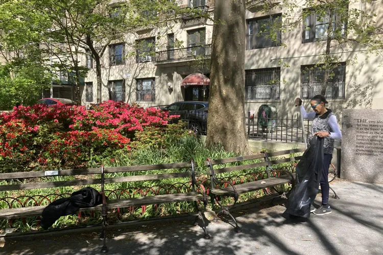 Person collecting garbage in Riverside Park North near benches and a garden bed.