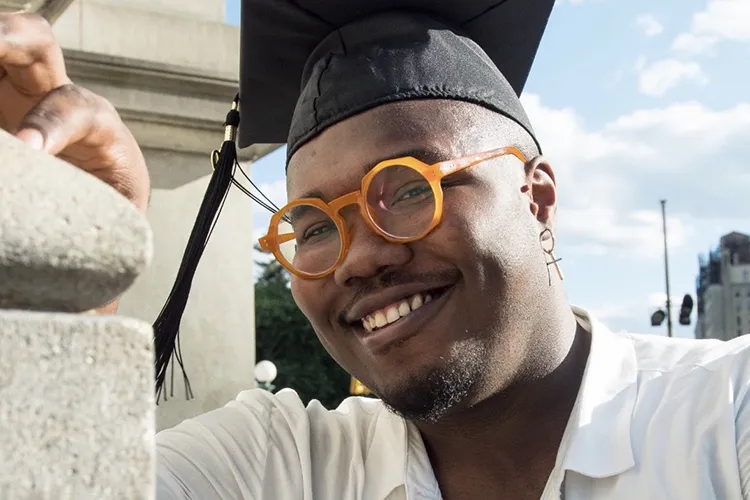 A young man wearing a graduation cap poses for a photo. 