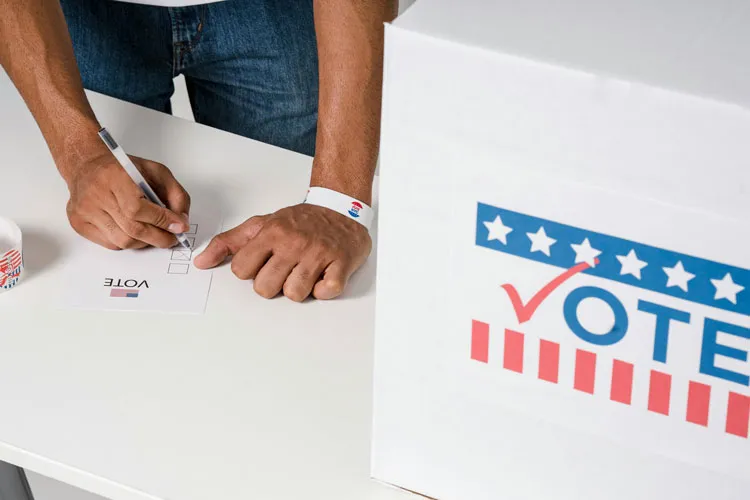 Someone writing something on a ballot next to a voting box.