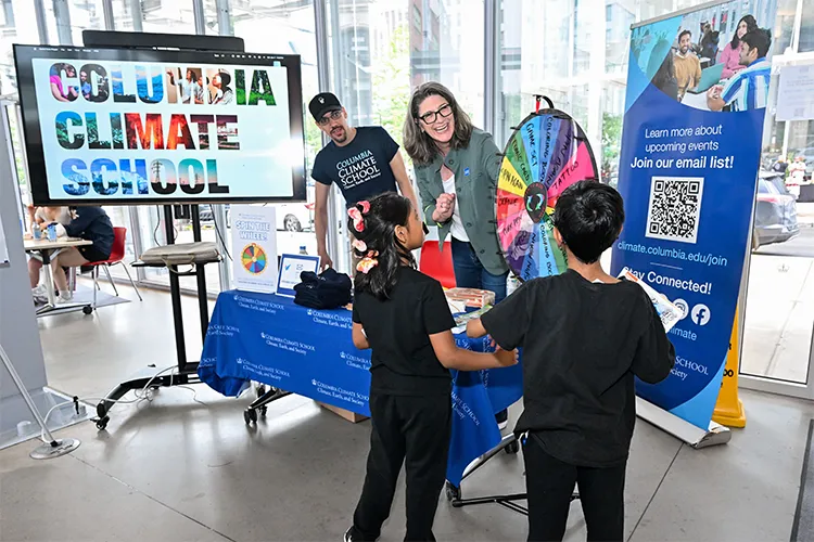 Two kids spin a wheel at a table staffed by two Columbia Climate School employees. 
