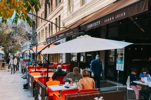 People sitting at sidewalk tables on Broadway at Community Food & Juice.