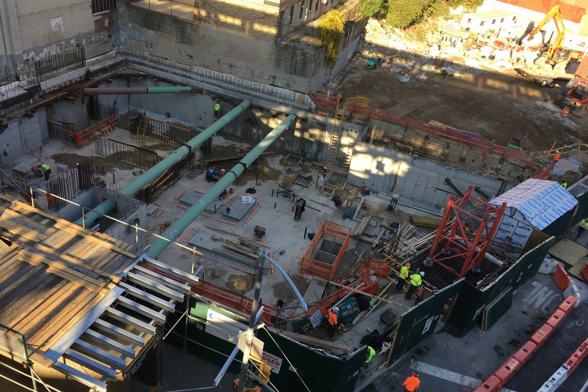 A aerial view of the 600 W. 125th Street construction site, full of materials and large green pipes running overhead.
