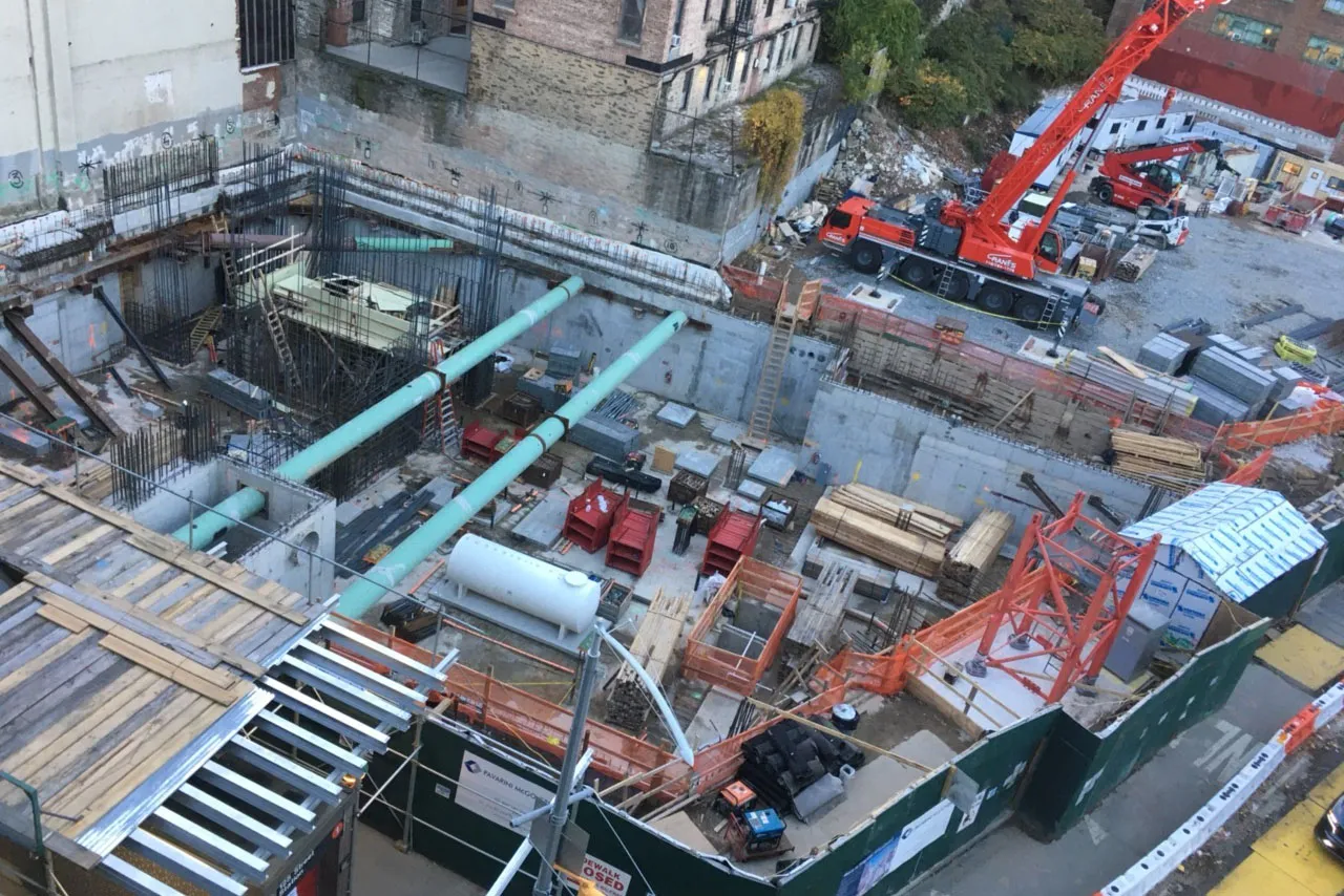 A aerial view of the 600 W. 125th Street construction site, full of materials and large green pipes running overhead. 