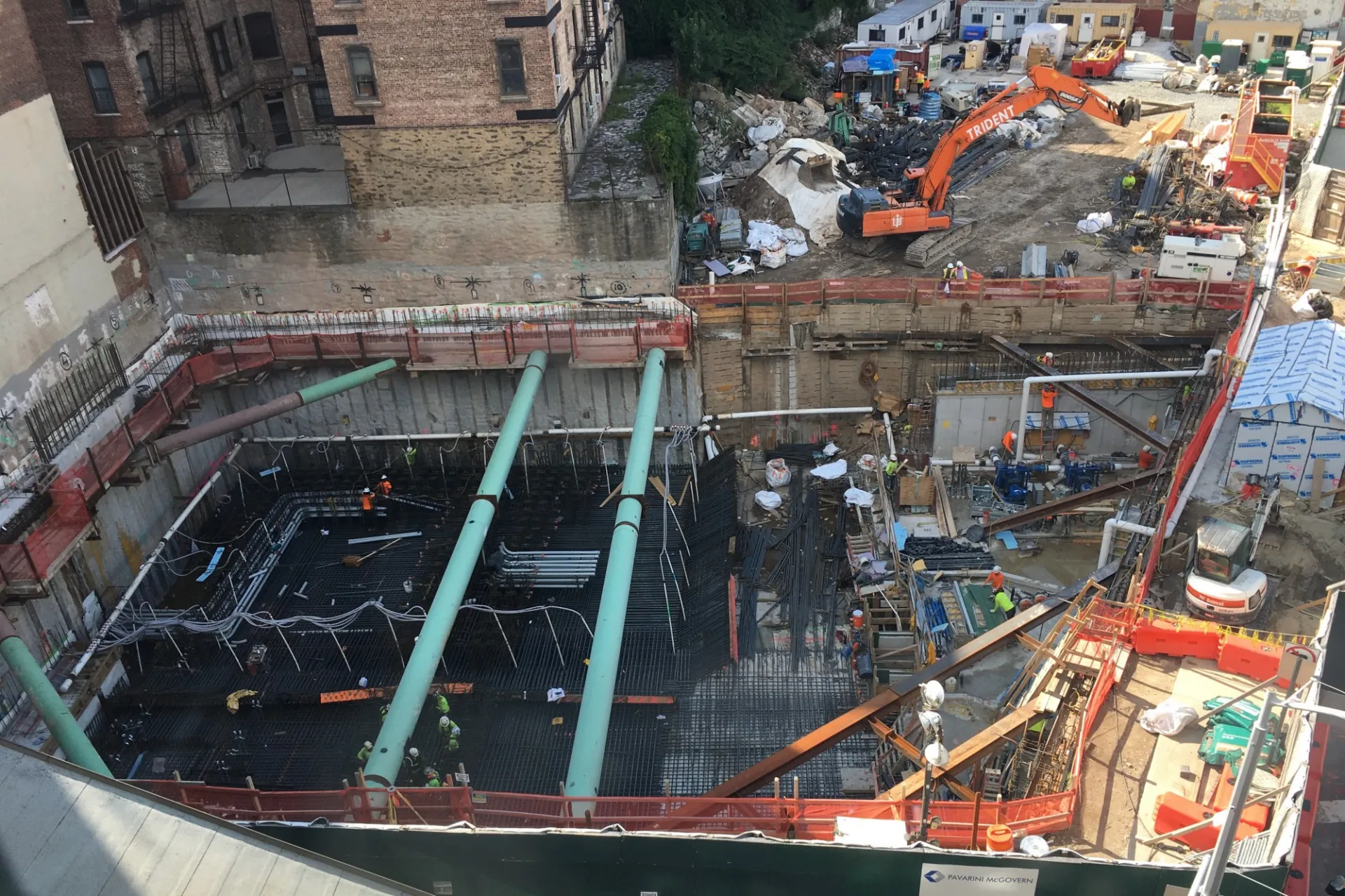 An aerial view of the 600 W. 125th Street construction site, with rebar covering half of the site, green pipes overhead, and equipment on the other half to perform foundation work.