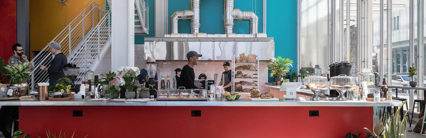 A view of the counter at Dear Mama, which is red with a teal accent wall, and has a selection of pastries available.