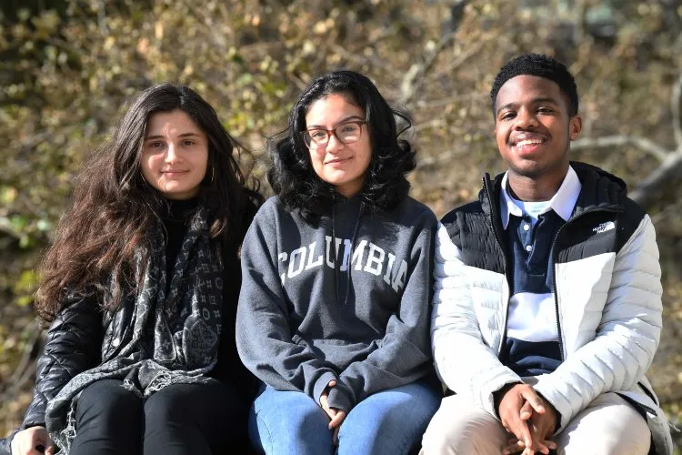 Two young women and a young man, all dressed warmly and sitting next to each other.