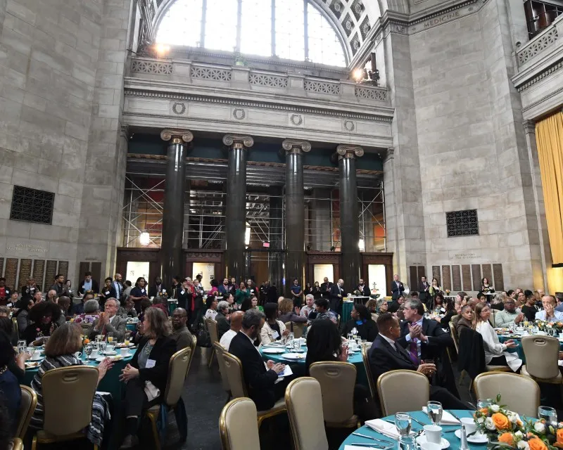 Local Community Members seated at round tables, networking. 