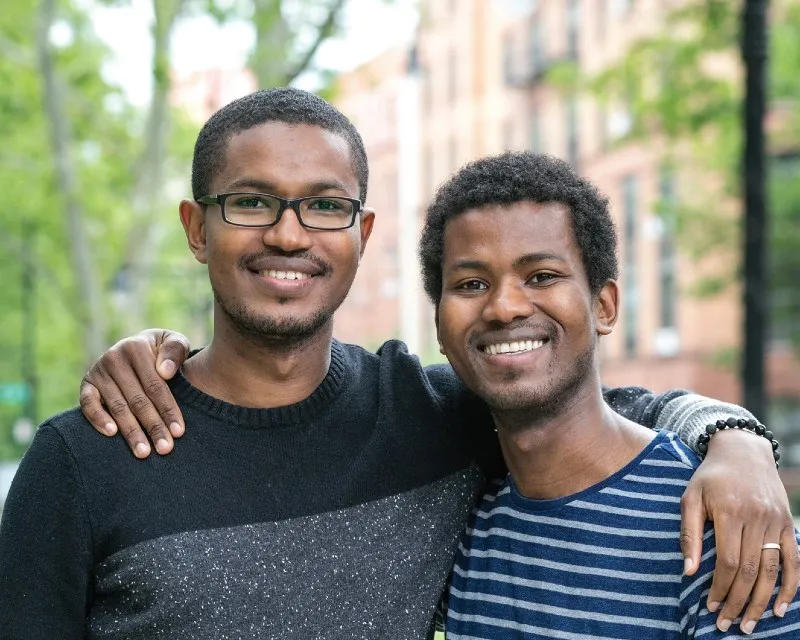 Two brothers smiling and posing for the camera outside.