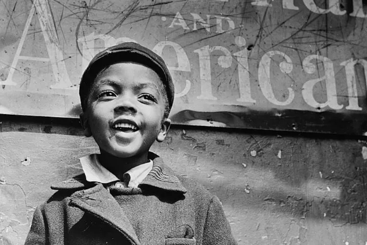 A boy in a cap and peacoat looks out from a sign that reads "American"