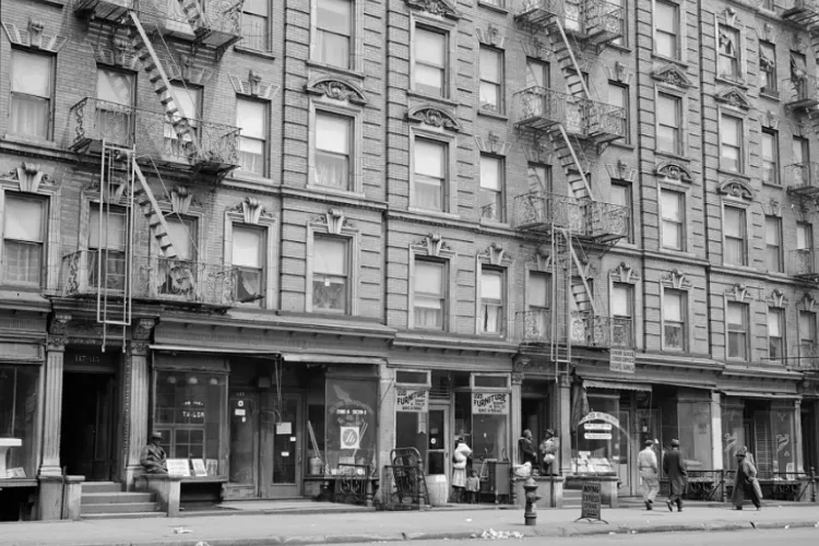 A row of Harlem apartment houses with fire escapes and people walking on the street
