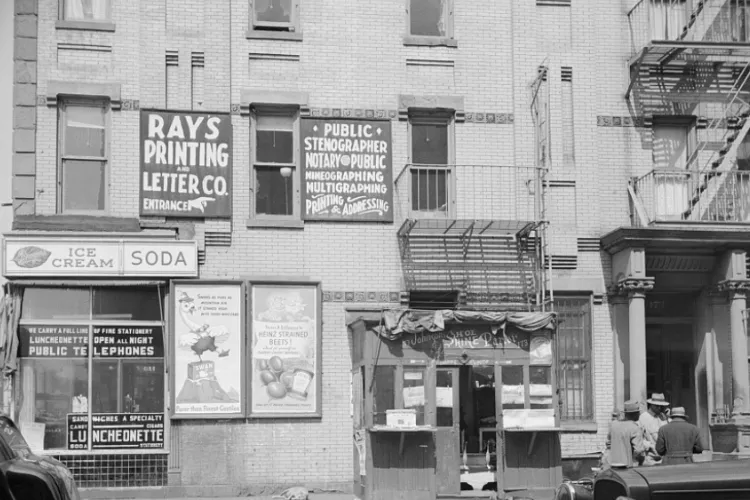 Store fronts in Harlem in the 1940s with signs like "Ray's Printing" and "Public Stenographer"